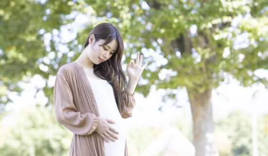 屋外でお腹に手を添えて立つ妊婦の後ろ姿